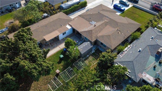 Aerial view of a single-story house with a brown roof, a detached structure, and a large green backyard with garden beds and trees.